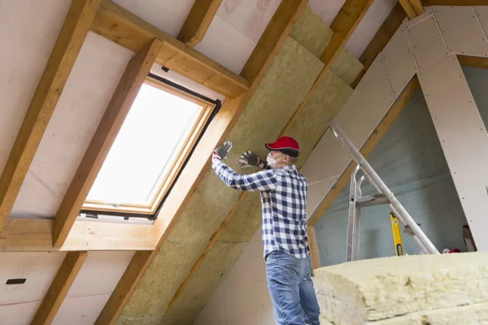 Installer fitting insulation beside a skylight in a roof space