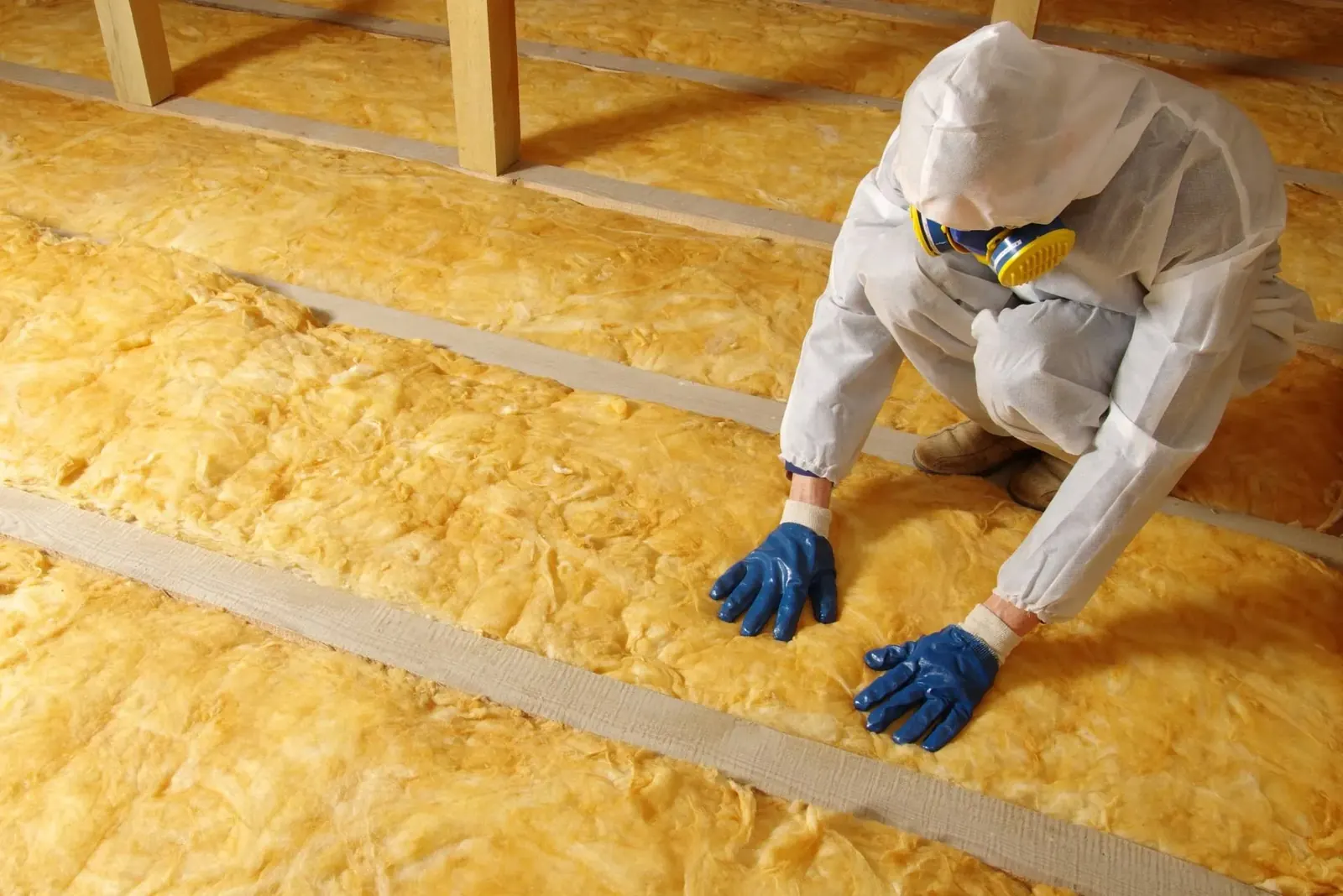 Installer laying glasswool batts between ceiling joists in a roof space