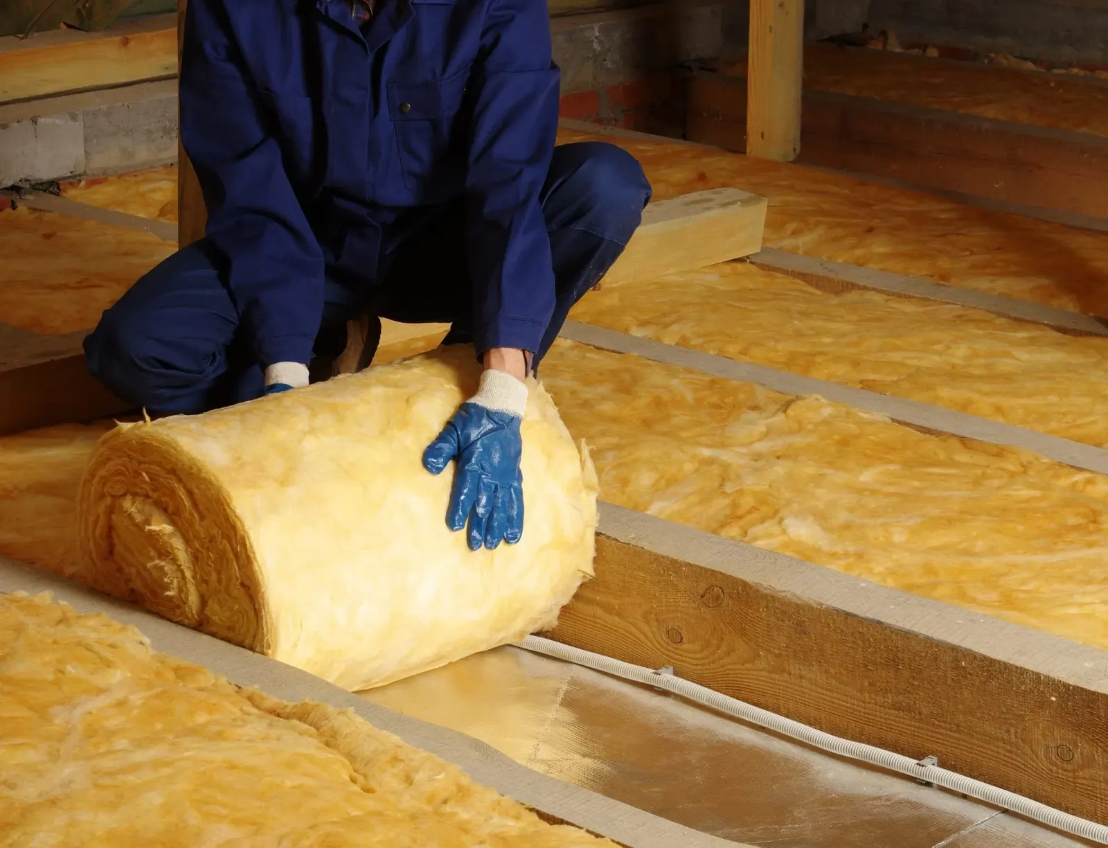 Roll of glasswool insulation being laid over foil in a roof space